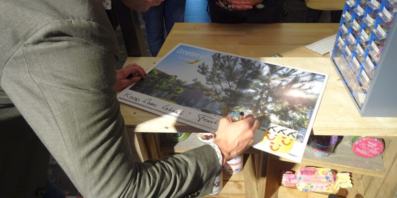 HR Frank van Wel (wethouder) tekent ansichtkaart bij Loon Lokaal